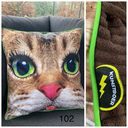  Cushion cover featuring a close-up image of a cat's head with large, vibrant green eyes and a pink nose. The cushion has a soft, plush texture and appears to be made of a brown and tan patterned fabric that resembles the fur of a domestic cat.