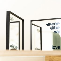 Set of two modern mirrors with black aluminum frames, available in 30x30 cm and 50x50 cm sizes, featuring text designs that read "All is Relative" and "Love". The mirrors come in different frame finishes including matte black, natural oak, and white oak.