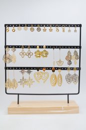 Lot de 16 paires de boucles d'oreilles assorties en acier inoxydable, présentées sur un présentoir métallique avec socle en bois.