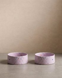  Two round, lilac-colored pet bowls with speckled patterns. Suitable for pet food or water.