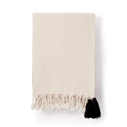 A cozy, cream-colored cotton weave blanket with black and white pom pom tassels along the edges.