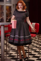 A retro-inspired black and white polka dot swing dress with a fitted bodice and a flared skirt. The dress features short sleeves and a classic silhouette.