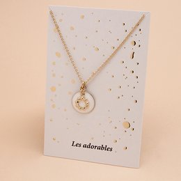 A gold-toned necklace with a large heart-shaped pendant featuring a floral design. The necklace is available in various color variants including Prusse, Ambre, Aniline, Corail, Blanc, Noir, Nude, Midnight Blue, Mousse, Brique, Sable, and Massaï.