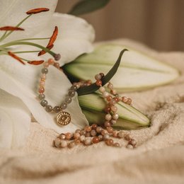 A beautiful sunstone mala necklace with intricate beadwork and a charm pendant. The mala features a mix of natural sunstone beads in warm tones, complemented by delicate floral accents.
