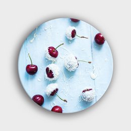  A round wall circle with a design of red cherries and chocolate and coconut accents on a light blue background.