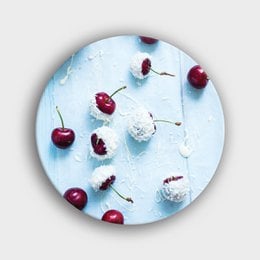 A round wall circle with a design of red cherries and chocolate and coconut accents on a light blue background.