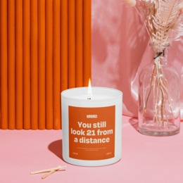 "Cozy Christmas scented candle with a playful 'You still look 21 from a distance' label. Made of natural wax, available in a variety of festive fragrances."