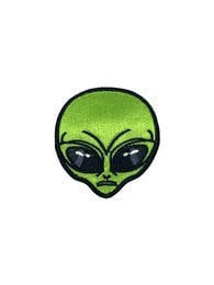 Alien-themed brooch with green alien head design, featuring a denim jacket with alien patches and pins.