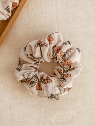 Vintage floral scrunchie with soft, delicate fabric and a scrunchie shape for holding hair. Features a mix of neutral and warm-toned floral patterns.