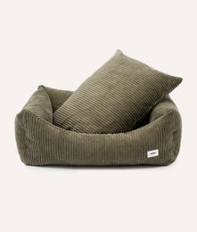 Soft, plush green corduroy dog bed with a small dog resting comfortably inside. The bed appears to be a cozy and comfortable place for a pet to relax.