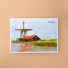 A6 postcard with envelope featuring a colorful illustration of a traditional Dutch windmill in a rural landscape. The postcard showcases the iconic architecture and natural scenery of the Zaandam region in the Netherlands.