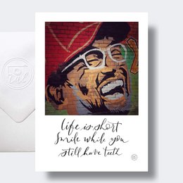 A colorful portrait of a smiling man with glasses, accompanied by the text "Life is short, smile while you still have teeth". This birthday card design features a vibrant, artistic style that captures the positive, lighthearted message.