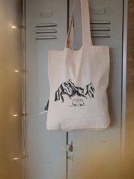Beige canvas tote bag with a printed mountain and camper design, suitable for everyday use or travel.