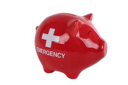A red ceramic piggy bank in the shape of a first aid cross, labeled "EMERGENCY". The piggy bank has a slot on the top for inserting coins.