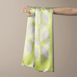 Dutches sjaal Suingu, a vibrant green and white patterned scarf made of a lightweight, silky material. The scarf features a striped design with a subtle abstract print, creating a stylish and versatile accessory.
