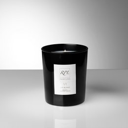 A tall, round, black candle with a white label that reads "VI - LYS BLANC". The candle is made of wax and has a wick in the center, indicating it is a scented candle.