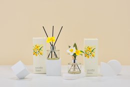 A tall, round glass diffuser bottle with a yellow daffodil flower and green leaves. The bottle is labeled "Cocodor" and contains a reed diffuser fragrance.