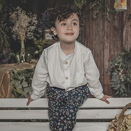 A white button-up shirt with long sleeves and a floral patterned skirt worn by a young child with curly hair.