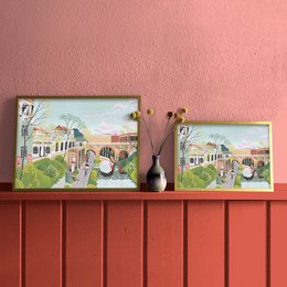 The image depicts a colorful, illustrated landscape of a canal with buildings, bridges, and people walking along the waterway. The description for this product could be: "Vibrant illustration of the Karl Heine Canal, featuring a scenic landscape with architectural elements, bridges, and people strolling along the water. Available in two sizes: 42 x 29.7 cm and 29.7 x 21 cm."