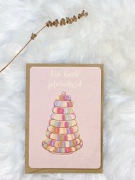 A colorful tower of macarons on a pink greeting card. The card features a decorative arrangement of macarons in various pastel shades, creating a whimsical and celebratory design.