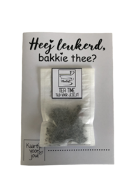 A greeting card with the text "Hey Leukerd, bakkie thee?" and a small package of tea leaves.