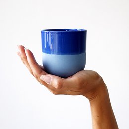 Porcelain cup in a deep blue color with a simple, minimalist design. The cup has a cylindrical shape and a smooth, glossy finish.