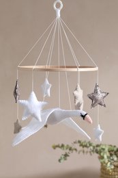 A mobile with white swan-shaped figurines suspended from a circular frame. The mobile features delicate, wispy strings that hold the swans in place, creating a serene and whimsical display.