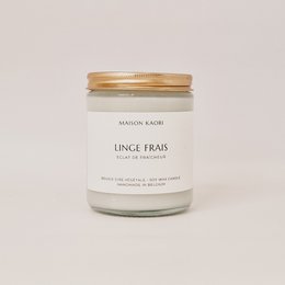 A tall, round white candle with a fresh linen scent, displayed with cotton branches in a white vase.
