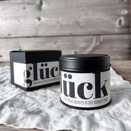 Tall, round, scented candle in a glass container with a black label that says "Zeit" in white text.