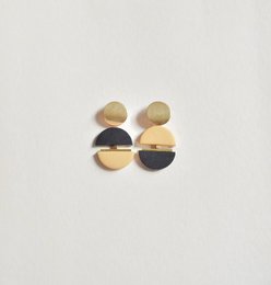 Statement earrings in contrasting black and mustard colors, featuring a bold, geometric design with circular shapes.