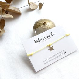 A yellow charm bracelet with a round, gold-colored charm featuring a star design. The bracelet is displayed on a white background with some natural elements like leaves or petals.