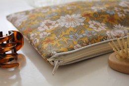 Beige floral clutch with zipper closure, made of fabric with a pattern of yellow, orange, and white flowers.