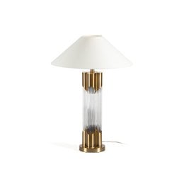 A tall, gold metal and transparent glass table lamp with a white shade. The lamp features a cylindrical shape with vertical glass panels and a gold metal base.