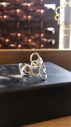 The Dione ring band in silver is a statement piece with a unique, abstract design. The ring features multiple overlapping circular shapes in a silver tone, creating a modern and eye-catching look. This ring would be a stylish addition to any jewelry collection.