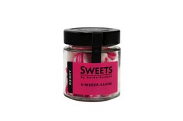 Raspberry cream bonbons in a glass jar with a black lid. The bonbons have a pink and white color and appear to be soft and chewy.