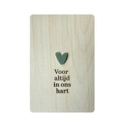 A wooden postcard with the text "Voor altijd in ons hart" (Forever in our hearts) and a heart-shaped embellishment. The postcard is displayed on a wooden shelf.