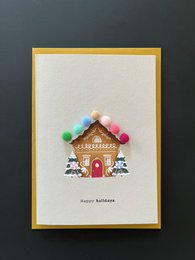 Colorful gingerbread house with pom-pom decorations, festive holiday card design.