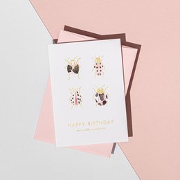 A pink and white birthday card with a playful beetle design and the text "Happy Birthday" in a stylish font. The card comes with a candy pink envelope.