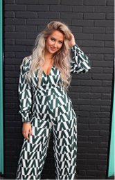 A long, green and white patterned jumpsuit with a deep v-neck and long sleeves. The jumpsuit has a relaxed, flowing silhouette and appears to be made of a lightweight, breathable fabric.