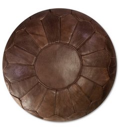 A large, round, chocolate-colored leather pouf with a sunburst pattern design. The pouf appears to be made of high-quality leather and would make a comfortable and stylish addition to a living room or bedroom.