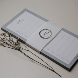 Gray notepad with minimalist design, featuring a to-do list and a circular icon.