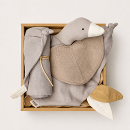  A soft, plush gray elephant-shaped gift box with a pacifier, bib, and blanket. The gift set is designed for babies and young children, featuring neutral colors and natural materials.