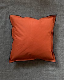 Rust orange solid cushion cover with dark piping trim, square shape, modern minimalist design.