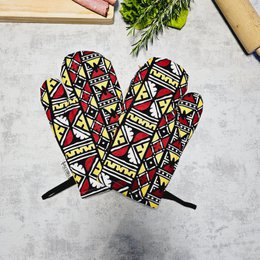 A pair of handmade oven gloves featuring a vibrant Bogolan print inspired by traditional African textiles. The gloves have a bold, geometric pattern in shades of red, yellow, and black, with a sturdy construction for heat protection in the kitchen.