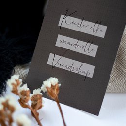A simple, elegant greeting card with the text "Cherish every friendship" handwritten in a cursive font against a dark background, accompanied by delicate floral accents.