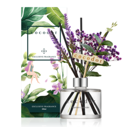 Lavender diffuser with glass container and purple floral arrangement on a table.

The image shows a lavender diffuser with a glass container and a purple floral arrangement on a table. The diffuser appears to be the Cocodor brand, as indicated by the product title. The floral arrangement includes purple flowers, likely lavender, and green leaves. The diffuser and floral arrangement are placed on a white surface, likely a table, with a potted plant visible in the background.