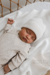 Soft, cozy merino wool baby bonnet in a neutral sand color. Features a warm, knitted design with ties to secure a snug fit.