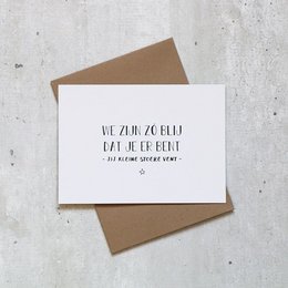 A white greeting card with a simple black text that reads "We are so glad you are here" on a brown envelope background.