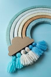Colorful rainbow-shaped wall hanging with tassels and wooden shapes, suitable for arts and crafts projects or home decor.