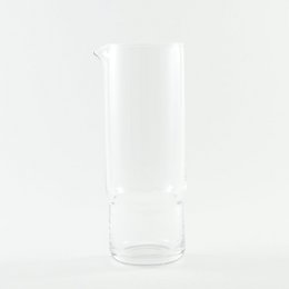 A tall, cylindrical clear glass carafe with a simple, minimalist design. The carafe has a sleek, elegant appearance and is suitable for serving water, juice, or other beverages.
